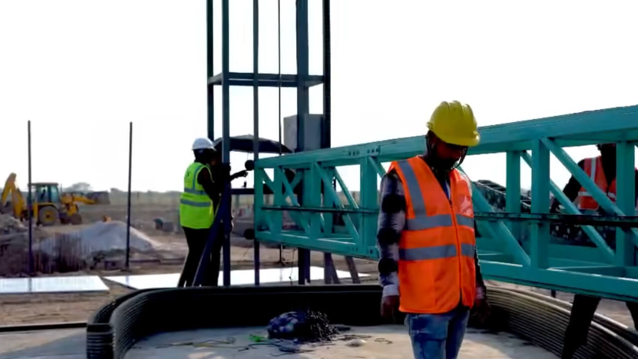 Workers alongside the gantry-mounted 3D concrete printer at the Dholera construction site.