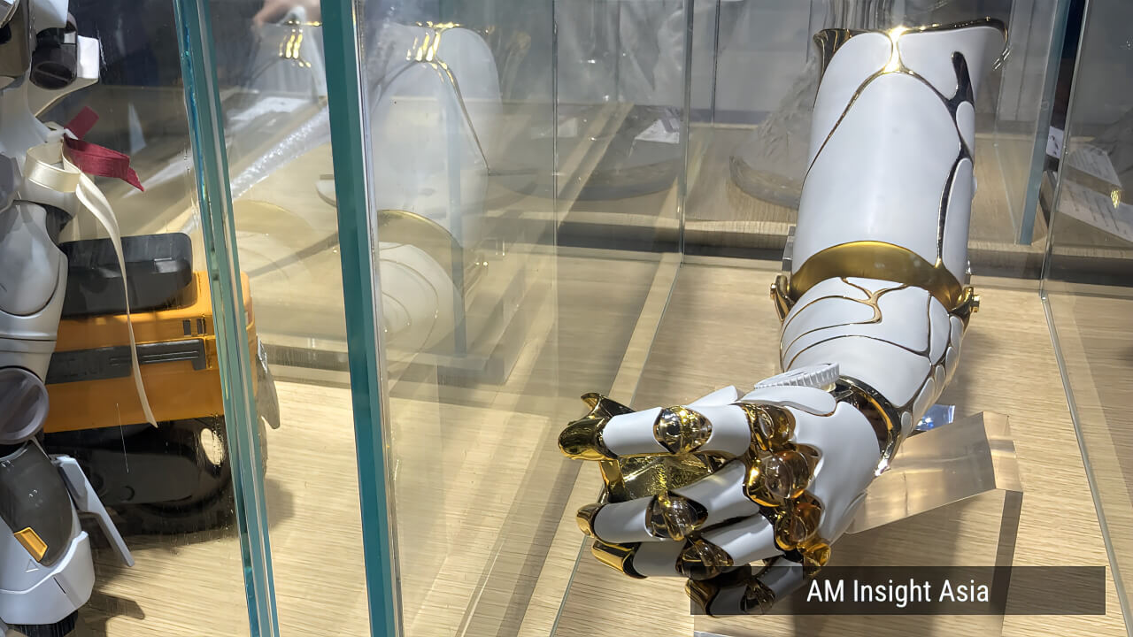 A white and gold mechanical arm at the HEYGEARS booth, showcasing the resolution of DLP photopolymer printing.