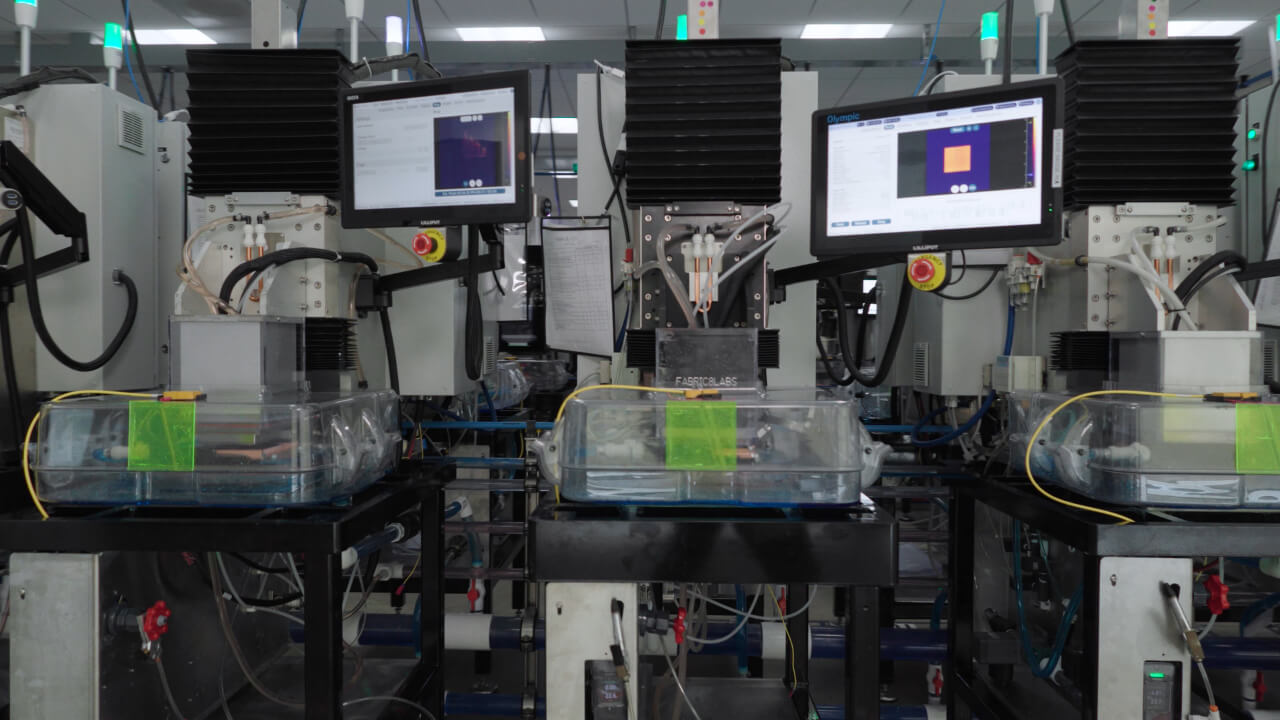 Close-up of an ECAM production line. Monitors display real-time thermal imaging and status data for each part being printed. | Video still: Fabric8Labs